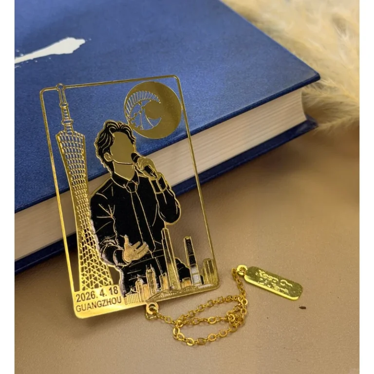 Gold-tone singer and skyline bookmark with a chain charm lying beside a blue book.