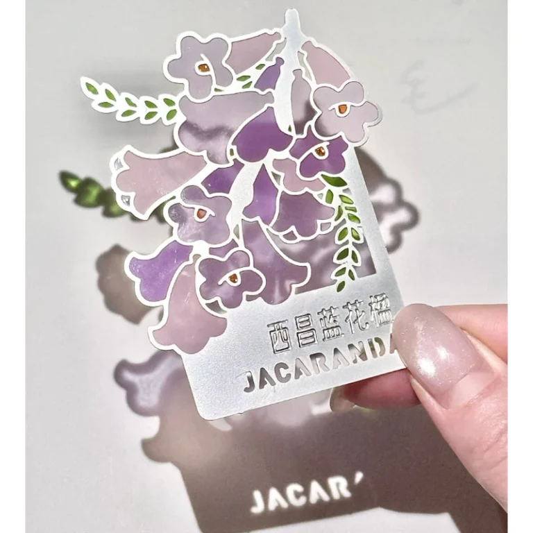 Purple flowering tree enamel metal bookmark with cut-out branches held in a hand.