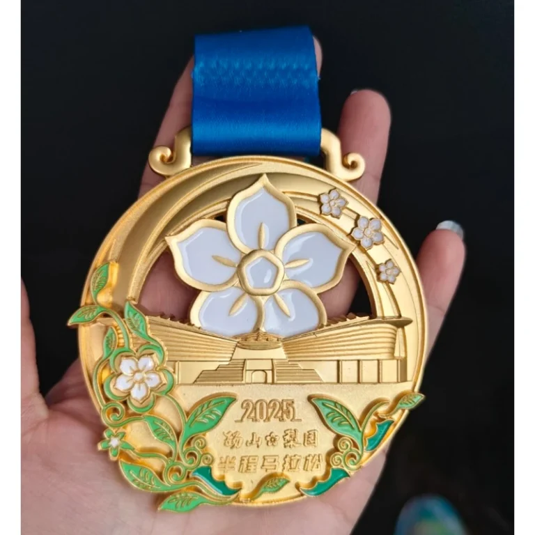 Gold-tone event medal with a flower, building details and blue ribbon.