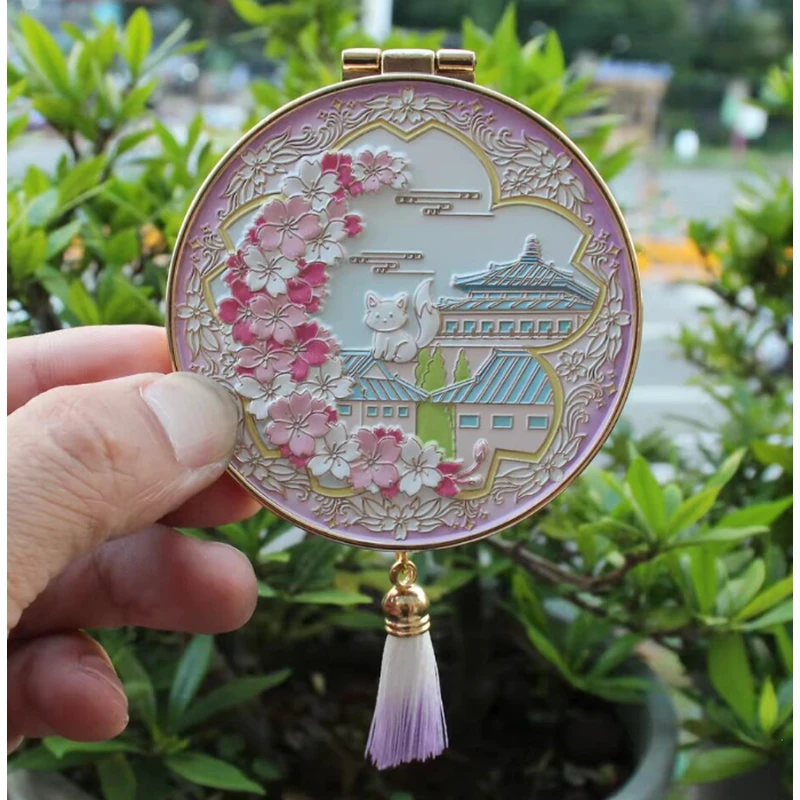Purple enamel compact mirror with Chinese architecture, cherry blossoms and a matching tassel.