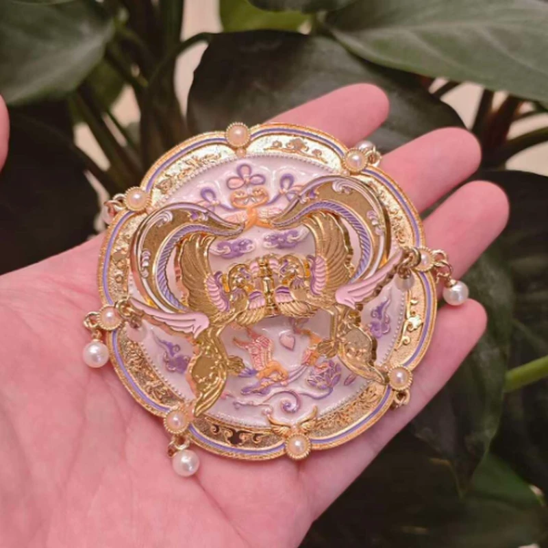 Pink and purple ornamental compact mirror with pearl details, held in a hand.
