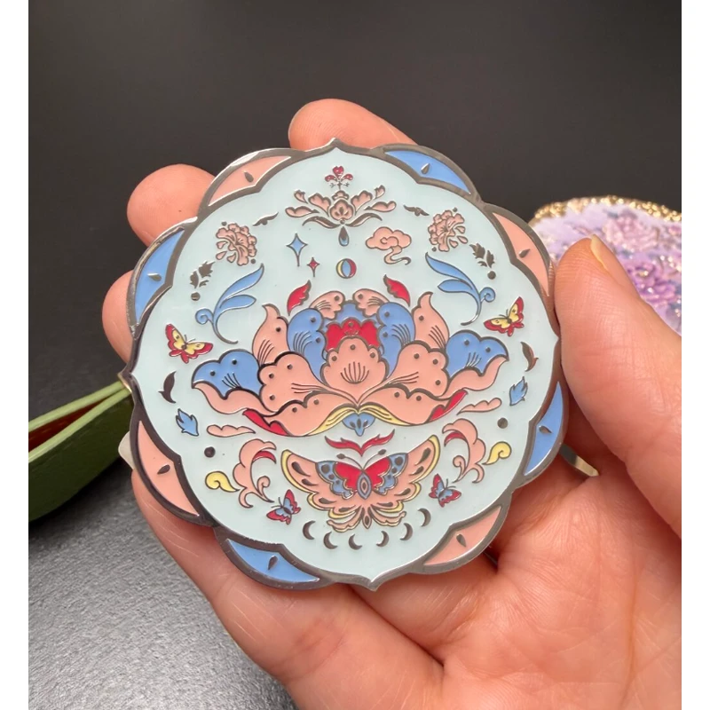Pale blue scalloped enamel compact mirror with colorful floral and character artwork.