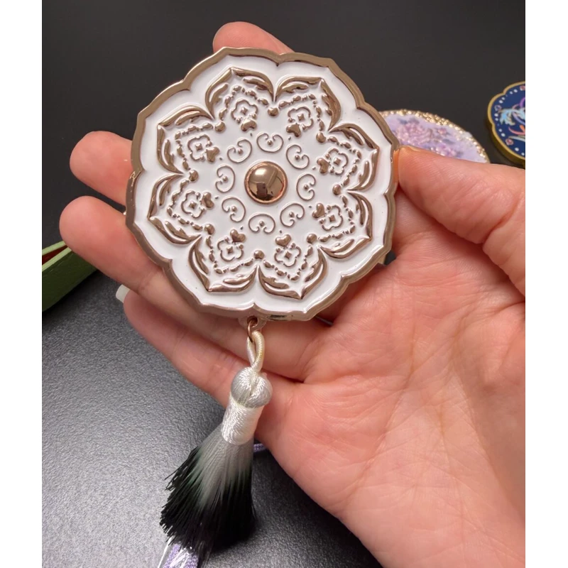 White ornamental flower-shaped compact mirror with sculpted relief and a black tassel.