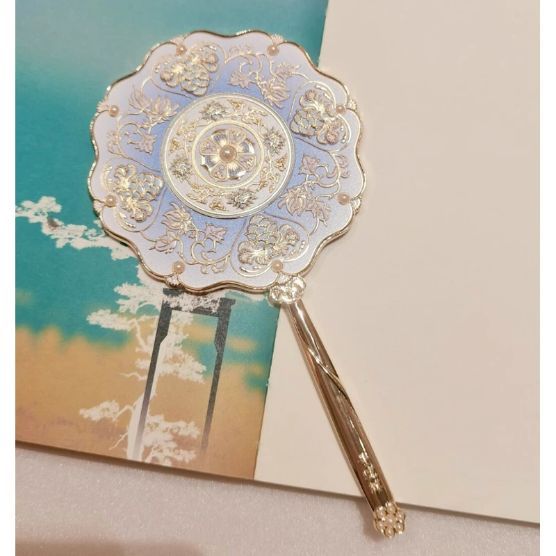 Blue and white scalloped handheld mirror leaning against decorative gift boxes.