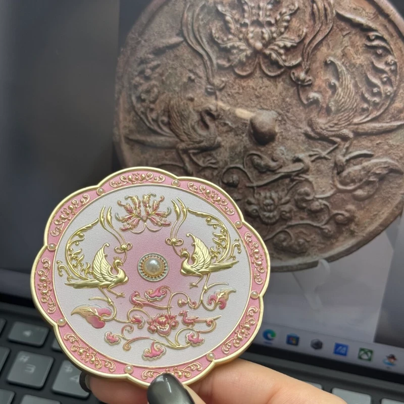 Pink round compact mirror with gold-tone ornamental relief.
